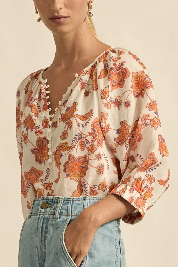 Woman wearing a floral blouse with orange and blue flowers on a beige background