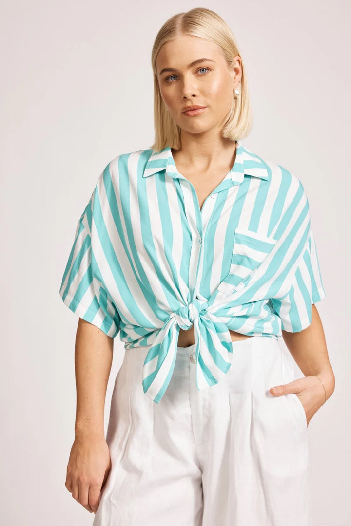 Woman wearing a turquoise and white striped shirt with a tied front, standing against a plain background.