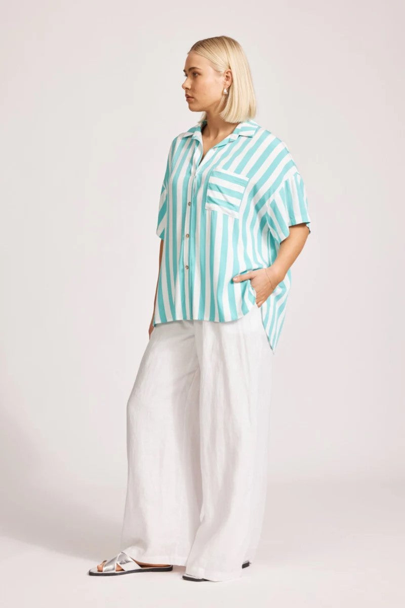 Woman wearing a turquoise and white striped shirt with white pants on a plain background