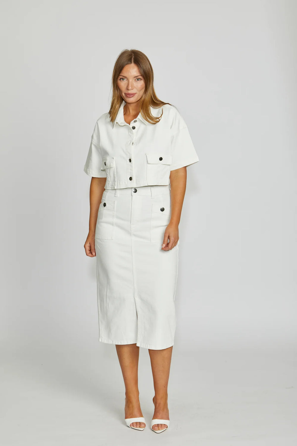 Woman wearing a white outfit with black buttons on a plain background
