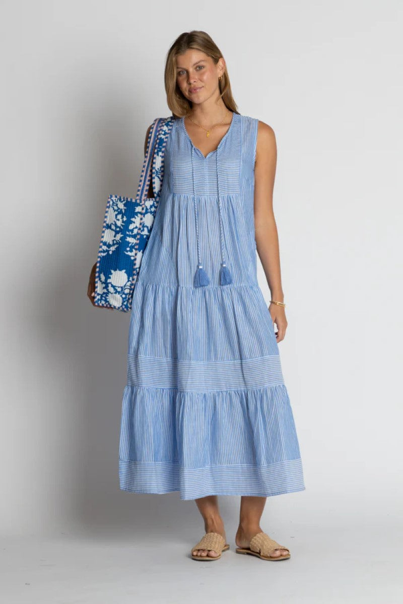 Woman wearing a blue dress holding a matching bag against a plain background