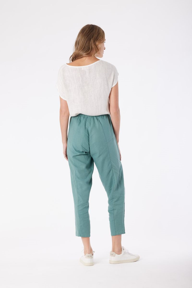 Woman wearing a white top and teal pants on a white background