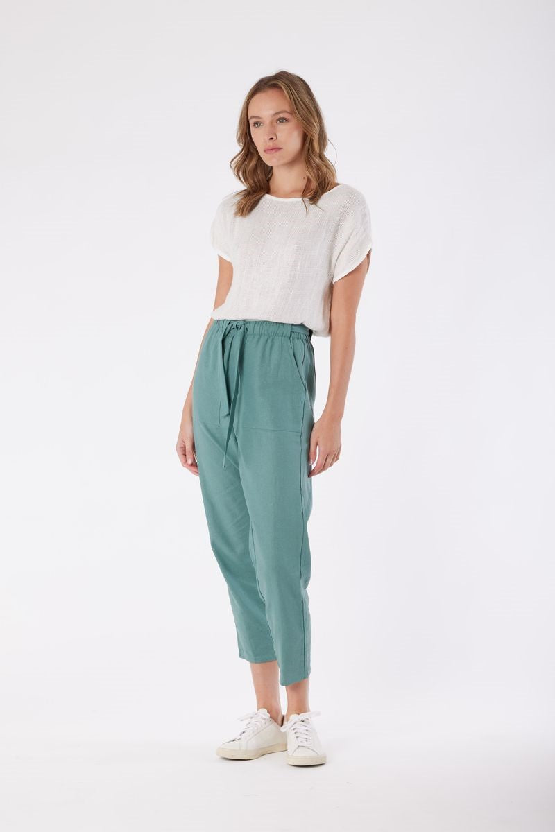 Woman wearing a white top and teal pants on a white background