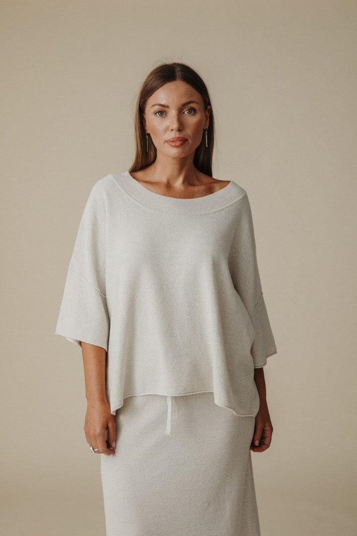 Woman wearing a light gray top and pants against a beige background