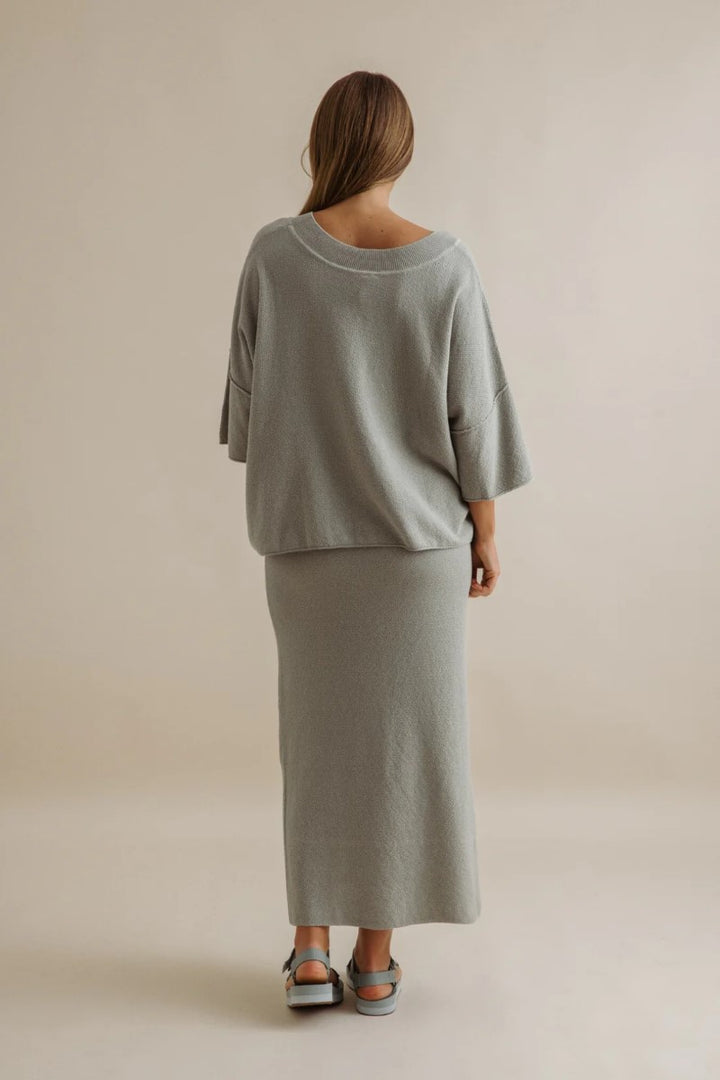 Woman wearing a gray outfit standing against a beige background