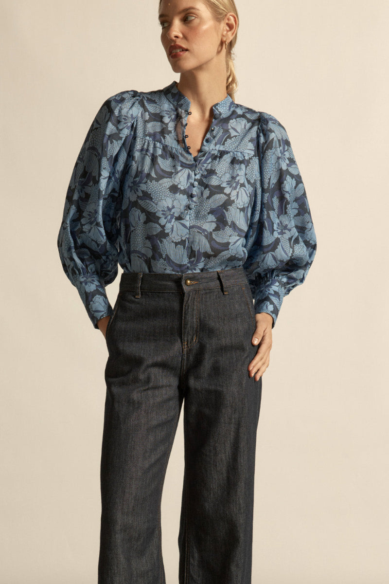 Woman wearing a floral blue blouse  front buttons black jeans on a beige background