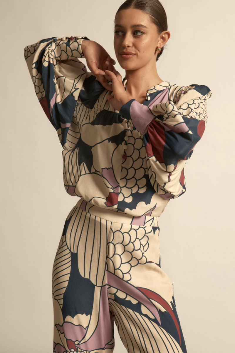 Woman wearing petals print with purple, red and blue accents paired with pants on a beige background