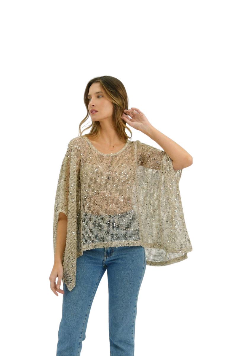 A woman modeling a sheer, open-knit top covered in shimmering sequins, paired with blue jeans, against a plain white background.