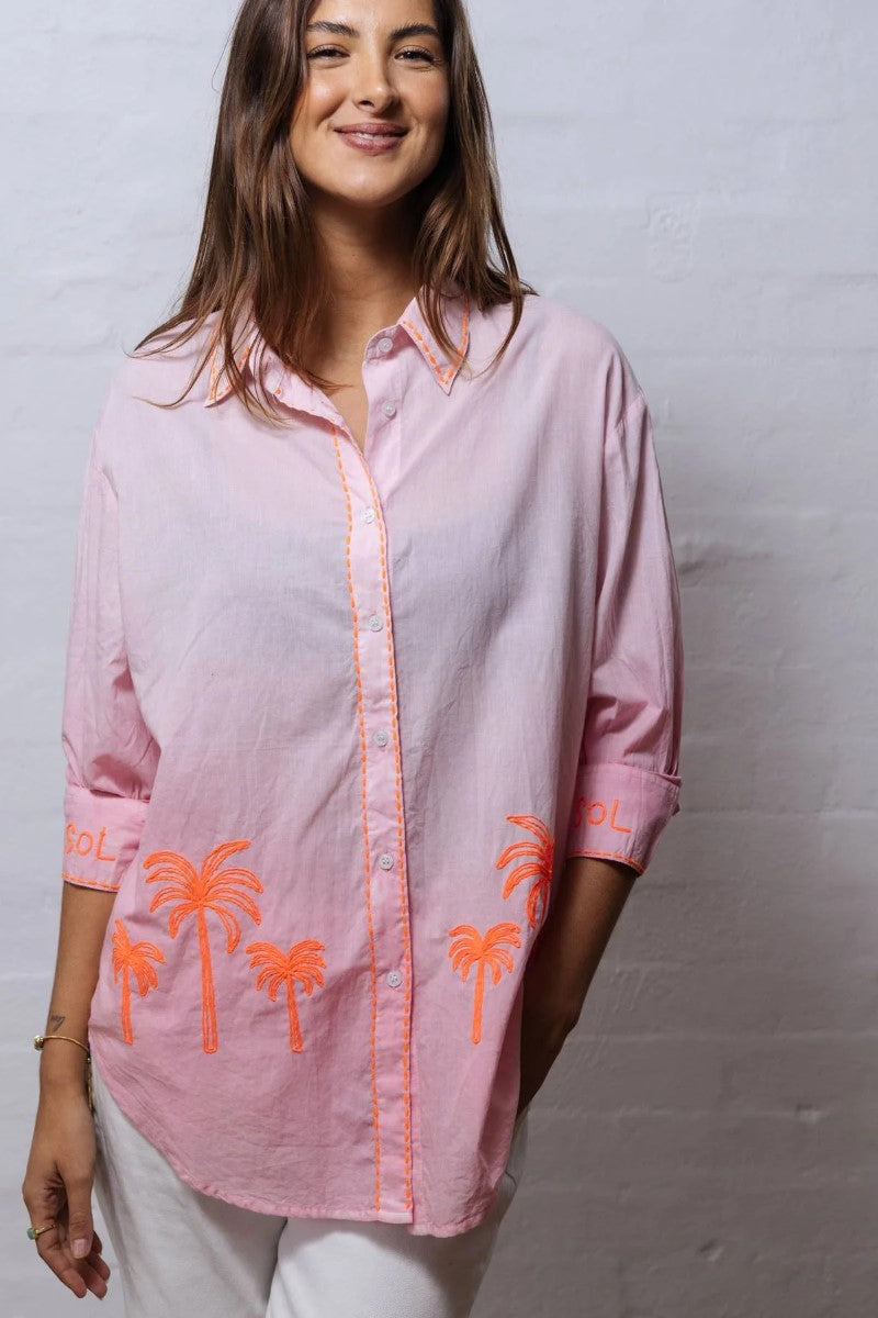 Woman wearing a pink shirt with orange palm tree designs against a plain background
