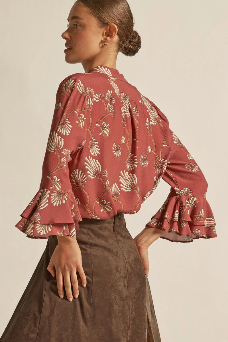 Woman wearing a red floral blouse with ruffled sleeves on a beige background