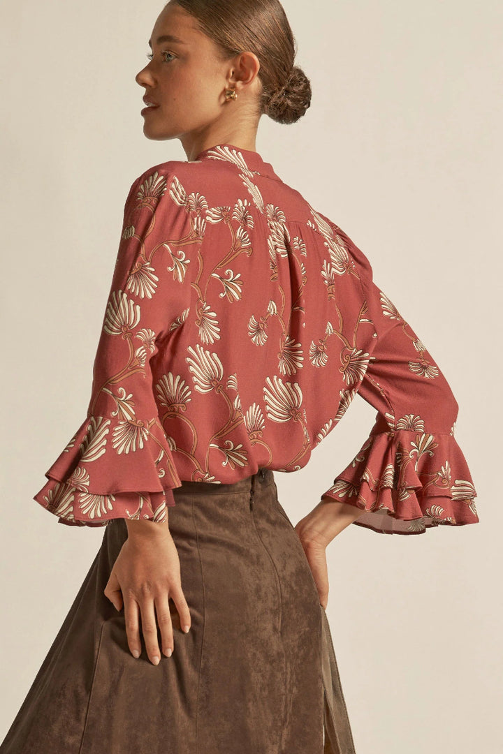Woman wearing a red floral blouse with ruffled sleeves on a beige background