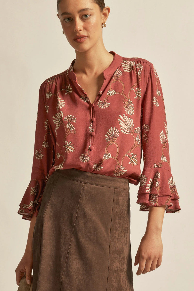 Woman wearing a patterned blouse and brown skirt against a beige background