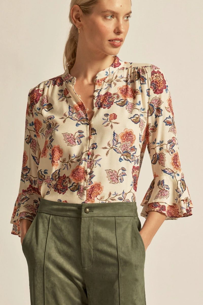 Woman wearing a floral blouse and green pants against a beige background