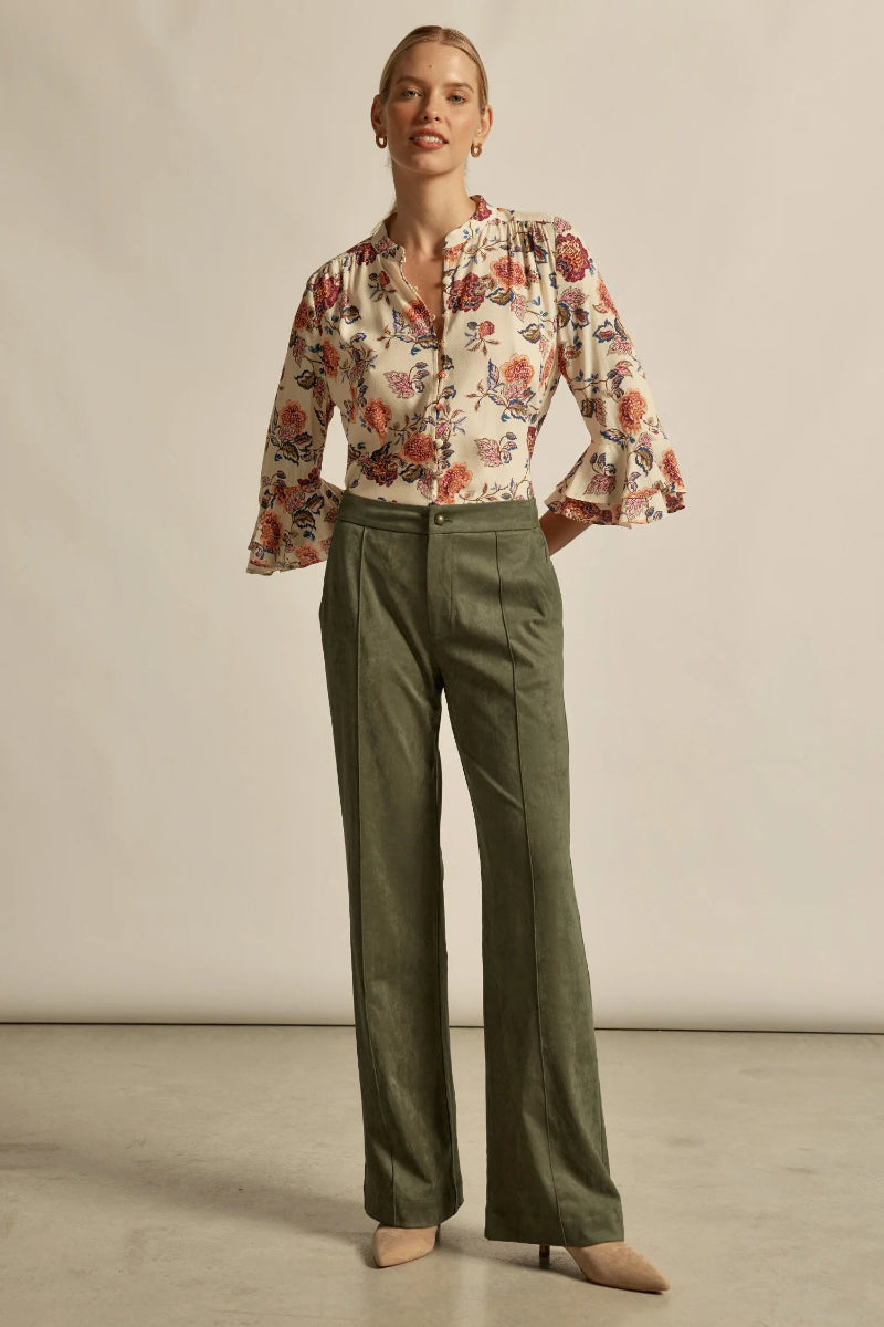 Woman wearing a floral blouse and green pants against a neutral background